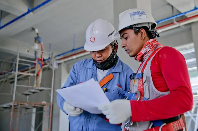 Picture of two engineers discussing plans, HVAC pipes are going in the background